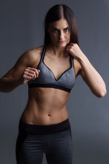 girl in gray sweatpants and top stands in a Boxing pose on a gray background.
