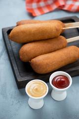 Closeup of corn dogs with mustard and ketchup over grey concrete background, vertical shot