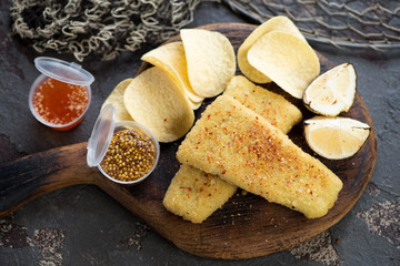 Fried breaded fish fillet with potato chips and dips on a rustic wooden serving board, studio shot