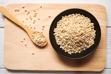Pearl barley grain in black ceramic bowl and wooden spoon on wooden plate and wooden background ,Top view perspective