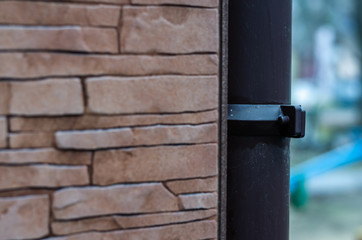 Brown drainpipe on the wall of a house. Focus on the bracket for fixing the pipe to the wall of the...
