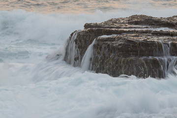 Rock with moss surrounded by wave water.