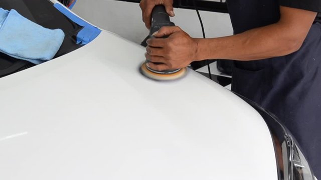 A man works at polishing the car after washing the car. Car polishing removes the scratches before waxing.
