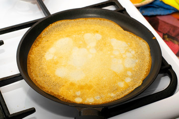 rosy pancake fried in a pan on a stove