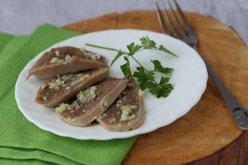 Sliced boiled beef tongue on white plate green napkin and wooden table with parsley garlic sauce, horizontal, copy space