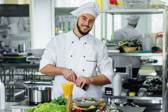 Professional bearded male, chef having fun and joy in a professional kitchen, preparing salade and spaghetti.
