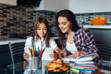 Mom helps daughter do her homework in the kitchen, trying to solve the task.