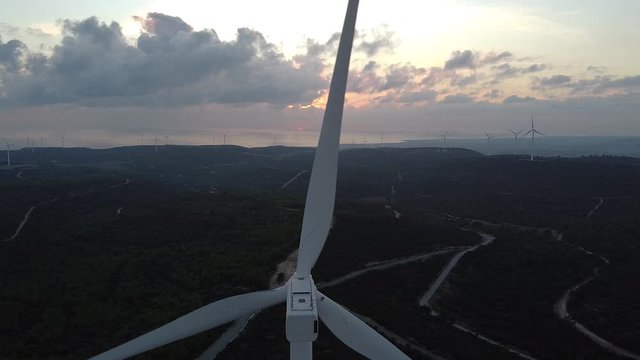 Close Rear View Of The Top Of A Wind Turbine As The Blades Spin Against A Sunset Sky, Showing The Mechanical Gear Box And Sensors As They Blink And Light Up.
