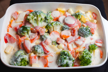 Sliced vegetables in a white ceramic bowl with white sauce. Preparation of baked vegetables. Close up view