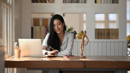 Portrait shot young woman looking at camera in home office.