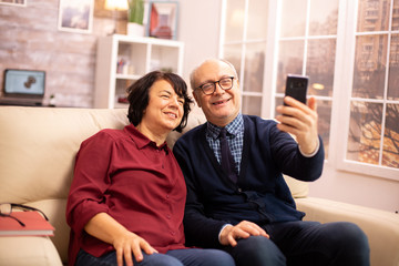 Obraz premium Beautiful elderly couple taking a selfie while sitting on the couch