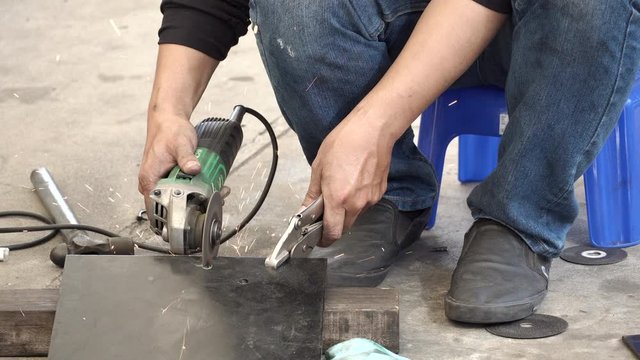 Male auto mechanic hand using angle grinder and adjustable spanner wrench for cutting steel plate from car part in auto repair garage. Automobile industry concept. 4K Video