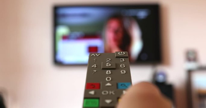 Man Hand Holding The TV Remote Control Of The Smart TV, Channel Surfing On The Blurred Internet Television In The Background. Close Up View - DCi 4K Video