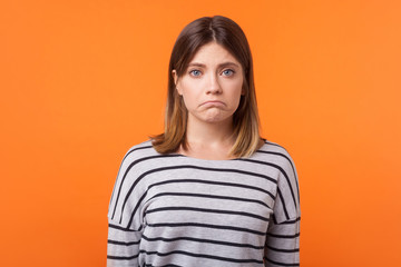 Portrait of upset young woman with brown hair in long sleeve striped casual shirt standing with...