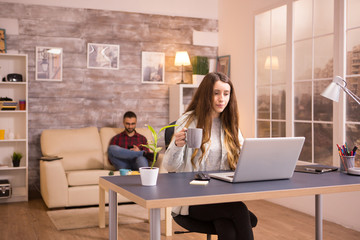 Beautiful female holding a cup of coffee while looking at laptop