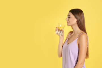 Young woman drinking lemon water on yellow background. Space for text