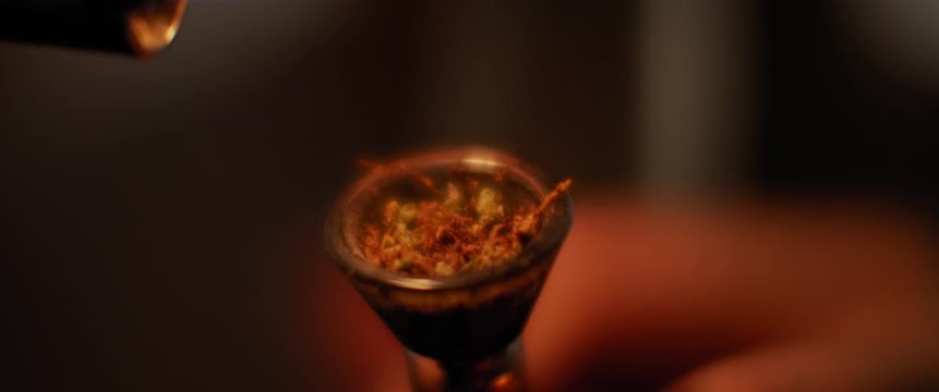 A person lighting up a glass bong of weed, the process of smoking medical marijuana. Dark room at night, close up, shallow depth of field, beautiful bokeh, cinematic shot with BMPCC 4K