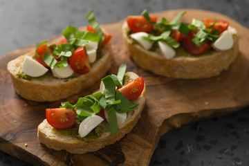 Bruschetta with mozzarella, cherry tomatoes and pesto on olive board