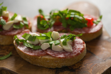 Bruschetta with mozzarella, cherry tomatoes and salame on olive board