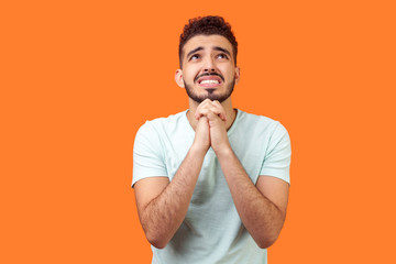 Please, I need help! Portrait of worried brunette man with beard in white t-shirt holding arms in...