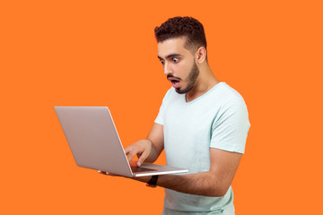 Portrait of young bearded man shocked by message on laptop, having troubles while working on...