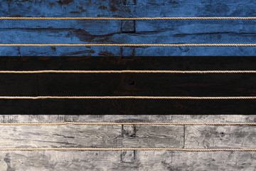 National flag  of Estonia on a wooden wall background. The concept of national pride and a symbol of the country. Flags painted on a wooden fence with a rope