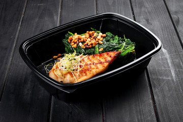 Chicken fillet with spinach and pine nuts in containers on a black wooden background. Takeaway....