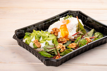 Poached egg with salad and nuts in containers on a white wooden background. Takeaway. Diet and healthy food.