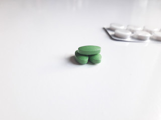 Miraculous and pernicious means. Hill of green pills in the focus in the foreground and blister pack with white tablets in the unfocused background