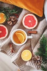Christmas cozy winter home decor. New year still life: cup of citrus tea, oranges, grapefruits, cinnamon sticks, pine cones, fir branches, knitted sweater. Flat lay, top view.