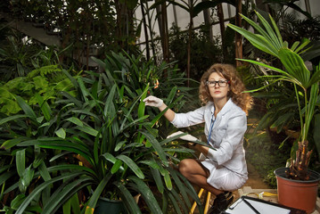 A scientist in a white medical gown cares for plants. Agrochemical in greenhouse of tropical...
