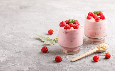 Yoghurt with raspberry and sesame in a glass and wooden spoon on gray concrete background. side view.