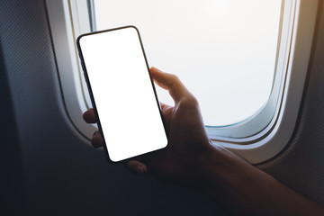 Mockup image of a hand holding a black mobile phone with blank desktop screen next to an airplane window