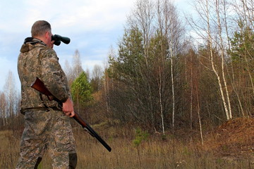 A hunter in protective clothing with a firearm observes the environment during the hunt.
