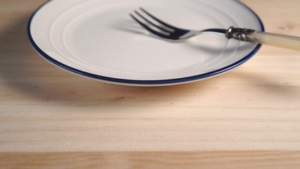 A white plate with a blue stripe around the edge of a close-up with a dessert fork. On a wooden background. Camera track