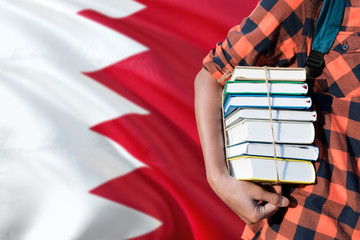 Bahrain national education concept. Close up of teenage student holding books under his arm with country flag background.
