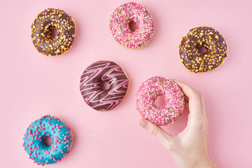 Woman hand take color donut on a pink background. Creativity minimalism style food concept, top view