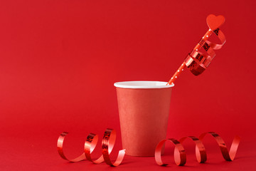 Paper coffee cup with wooden heart on straw and festive ribbons on the red background.  Valentines day concept
