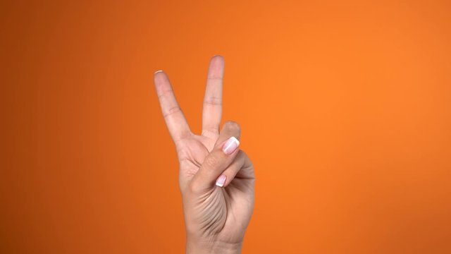 Closeup view of woman raising double fingers up. Peace and victory gesture. Real time 4k video footage.
