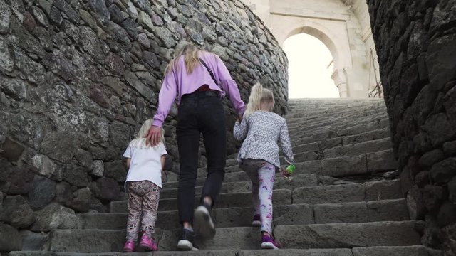 Young mother with two little daughters climbing on a wall of medieval castle