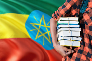 Ethiopia national education concept. Close up of teenage student holding books under his arm with country flag background.