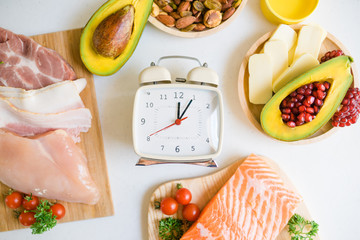 Intermittent fasting and Healthy food. Concept.Alarm clock and Keto diet food ingredients on white table.Ketogenic mean Low carb and High fat.