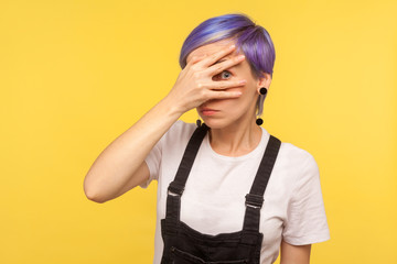 Portrait of nosy wondered hipster girl with violet short hair in denim overalls looking through...