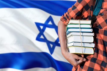 Israel national education concept. Close up of teenage student holding books under his arm with country flag background.