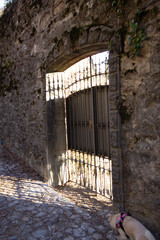 Cancello in ferro tra vecchie mura medievali rovinate in un borgo del lago di Como.