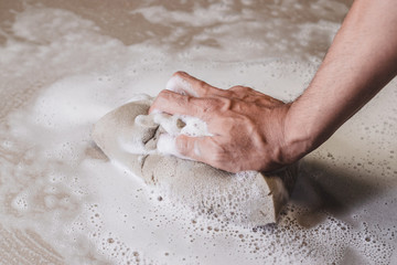Men's hands are using a sponge cleaning the tile floor.