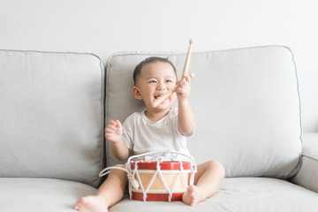 Little baby drummer boy playing and hitting the drum set at home.Asian boy playing and singing...