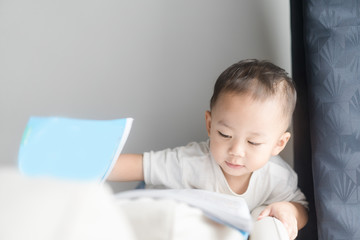 Fototapeta premium 2 years little asian toddler boy in white t-shirt reading bible picture story for kid in the morning.Hands holding on a Holy Bible in bed room concept for Education bible study, faith and religion.