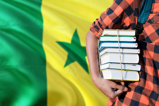 Senegal national education concept. Close up of teenage student holding books under his arm with country flag background.