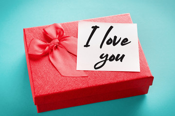 Red gift box with a note with the words "I love you" on a blue background